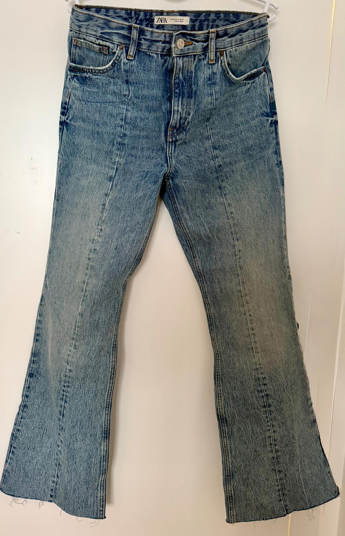 Blue denim flared jeans hanging on a white hanger. Visible label with the text "ZARA".