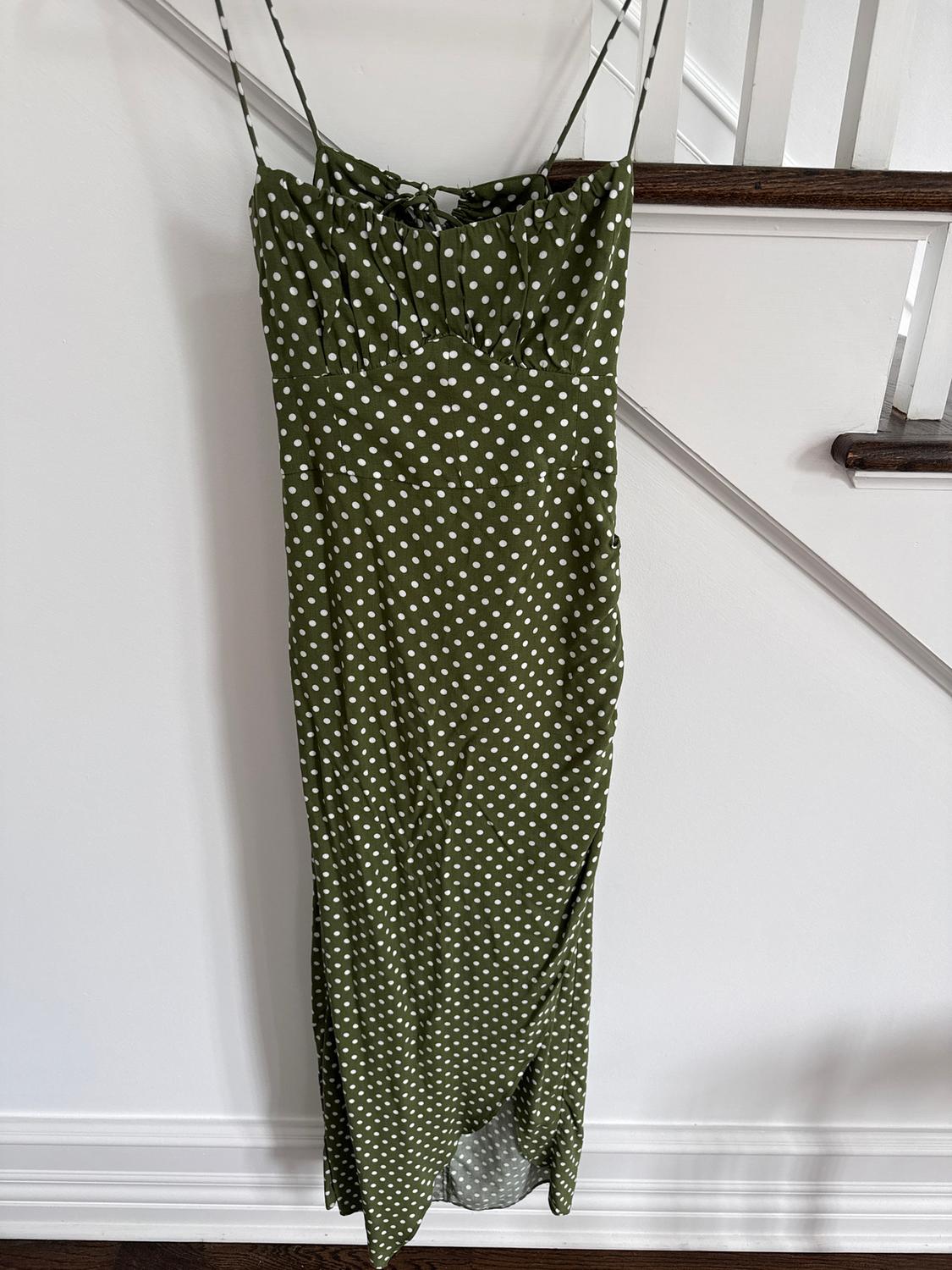 Long green dress with thin straps and a white polka dot print, hanging on a white stair railing.