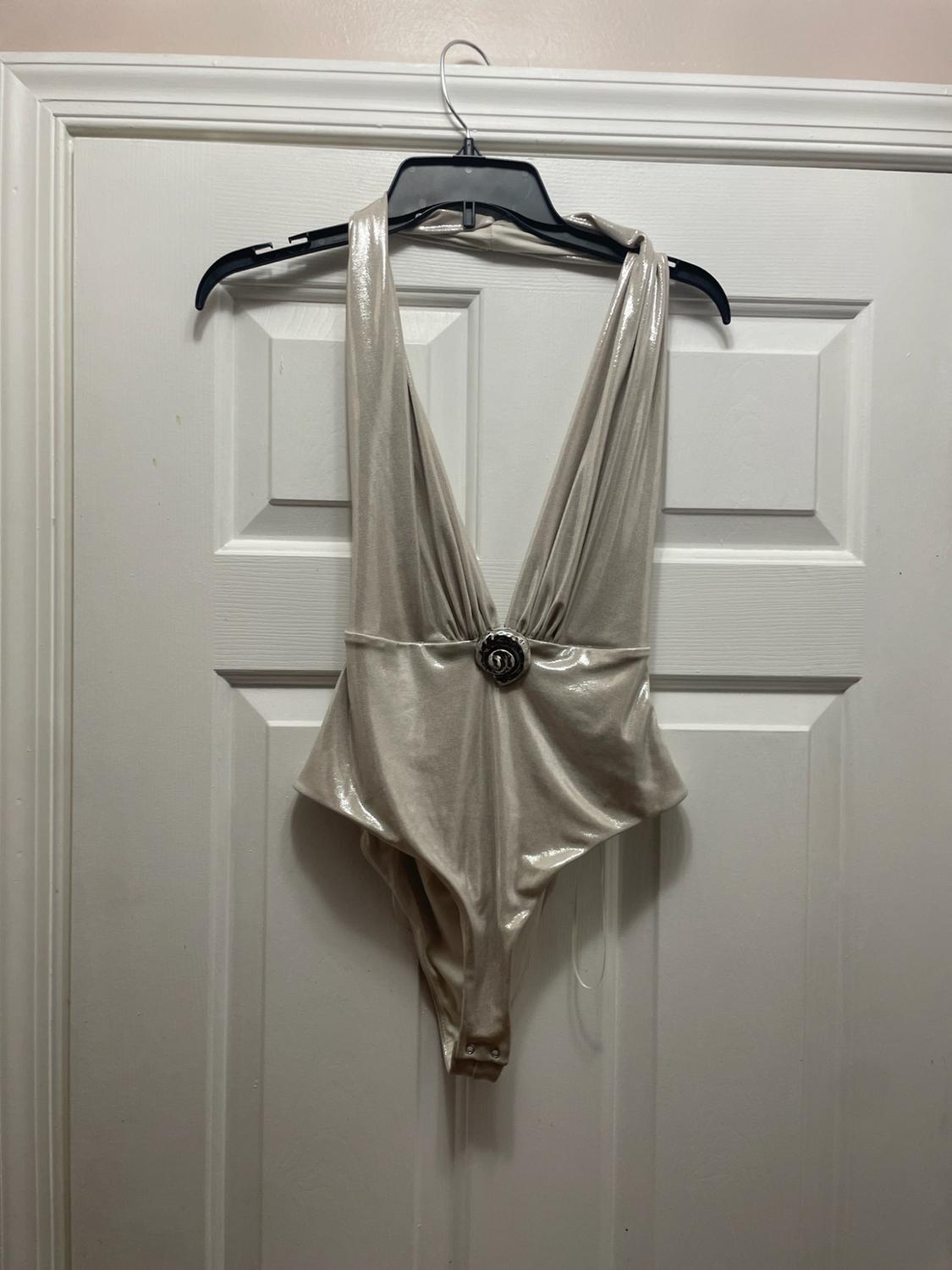 Metallic bodysuit with a deep V-neckline, halter neck, and waist appliqué, hanging from a black hanger on a white door.