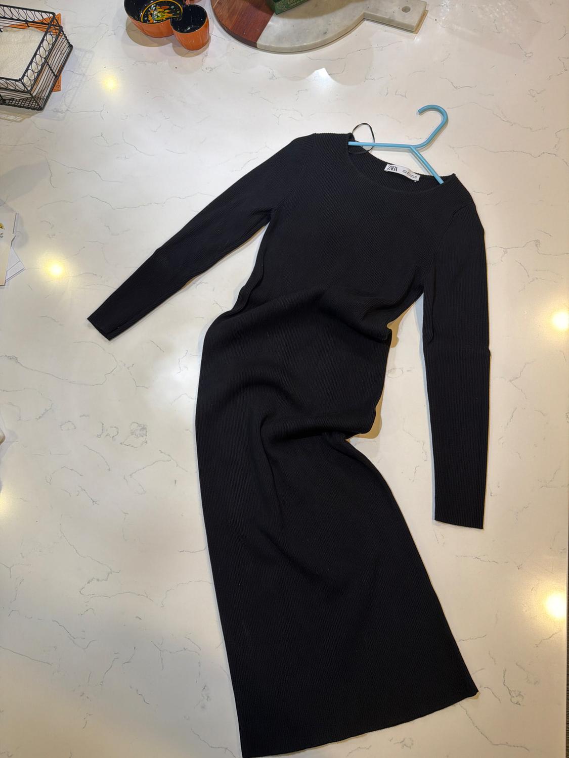 Long-sleeved black dress on a white marble table. The dress is hanging on a blue hanger.