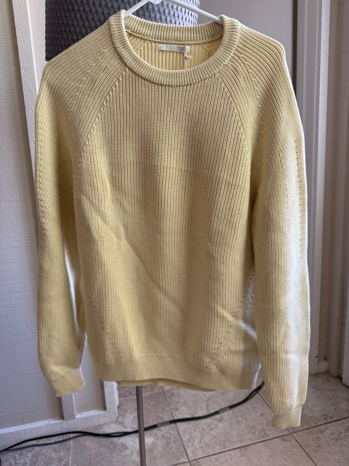 Light yellow ribbed knitted jumper with a round neck and long sleeves, hanging on a white hanger indoors.