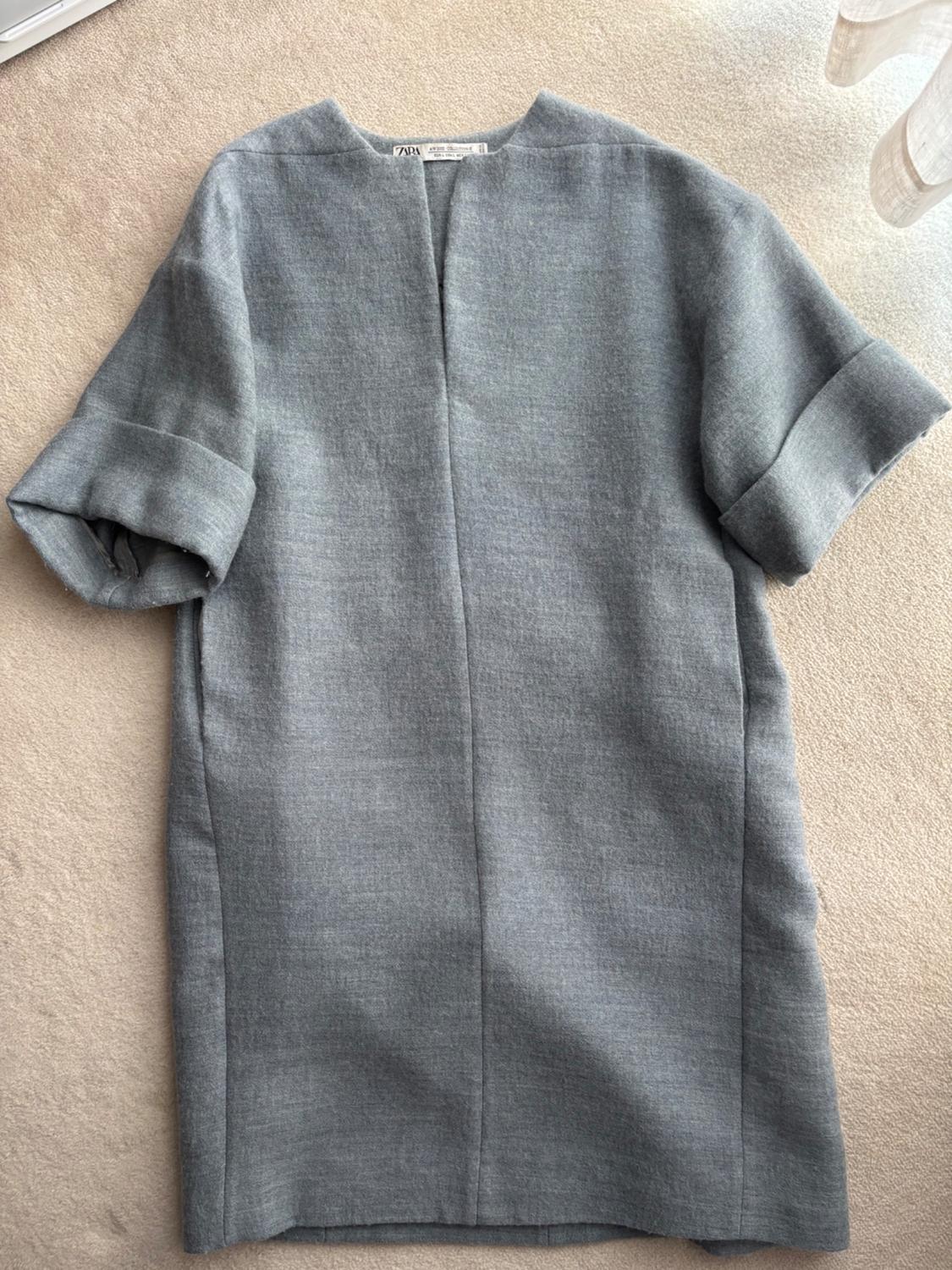 Grey, short-sleeved, round-neck dress on a beige surface. Visible label on the collar.