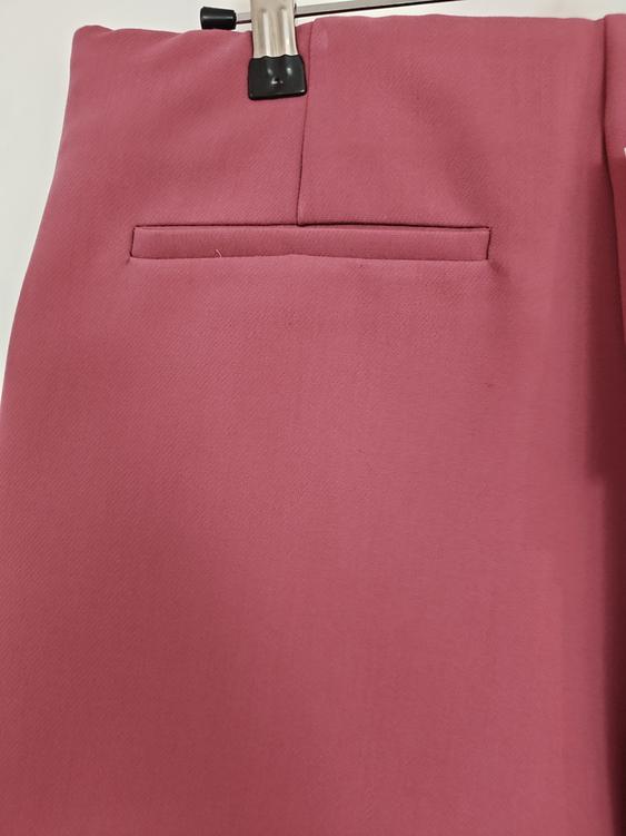 Pink trousers hanging on a hanger, showing a back pocket and stitching details. White background.