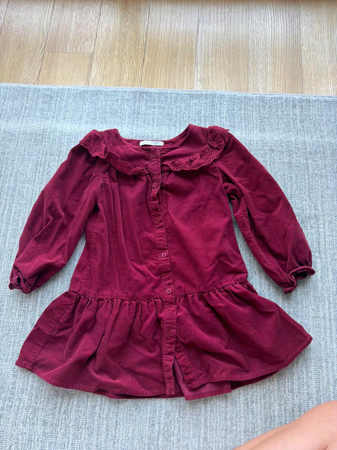 Burgundy long-sleeved dress with a lace collar and front buttons, on a grey rug and wooden floor.
