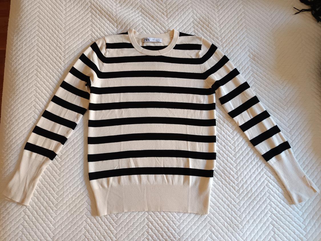 Black and white horizontal striped jumper on a white quilt with a herringbone pattern. Visible label on the collar.
