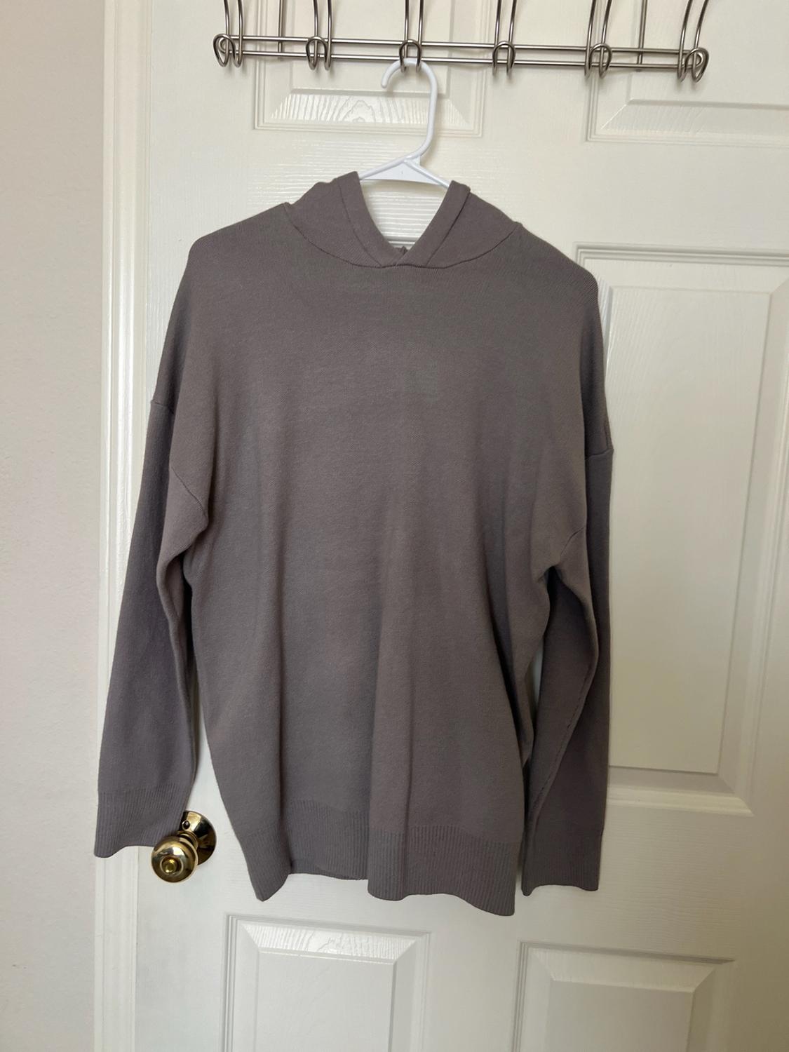 Gray knit hoodie hanging on a hanger over a white interior door. Casual and relaxed style.