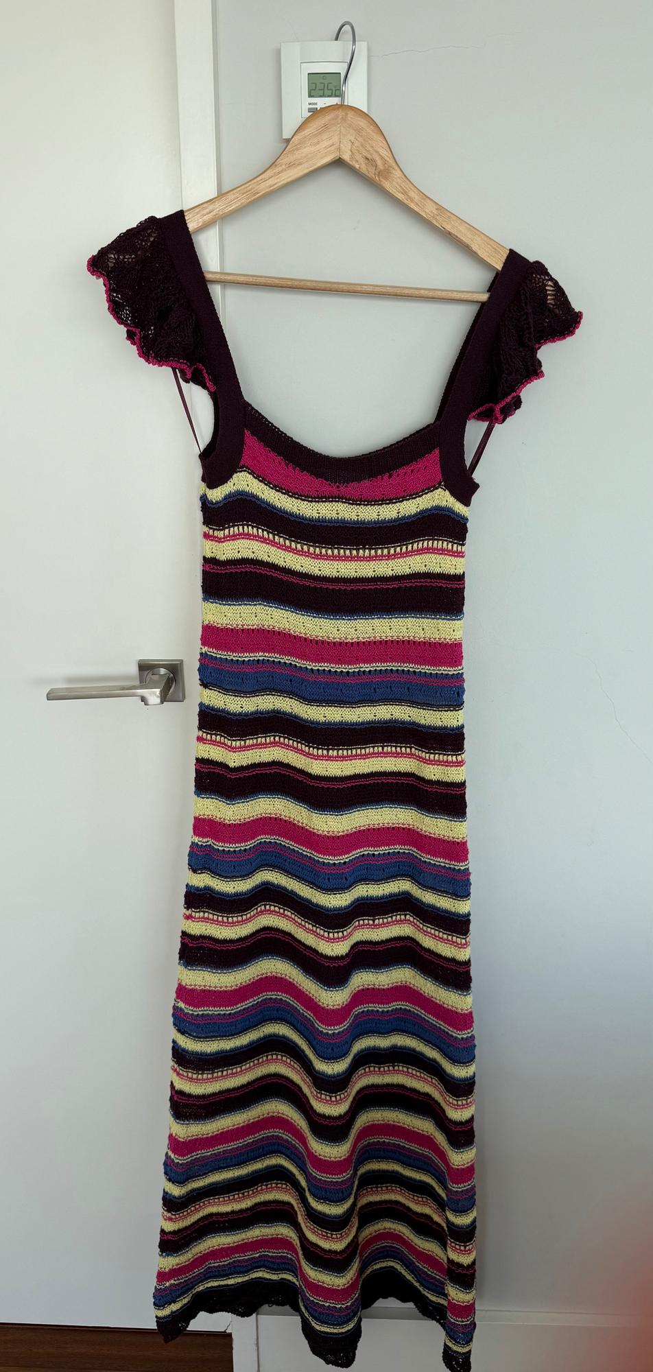 Knitted dress with straps and frills on the shoulders, hanging on a hanger. Striped design in shades of pink, blue and yellow.