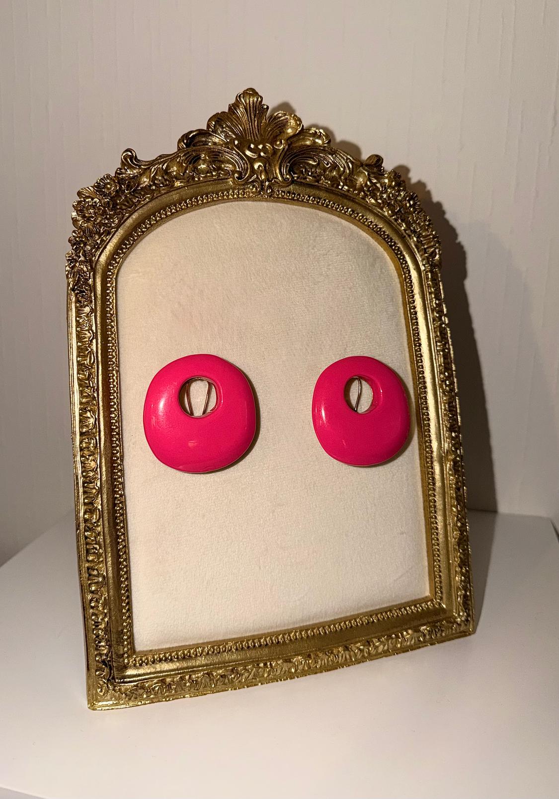 Bright pink round earrings in an ornate gold frame on a white background.