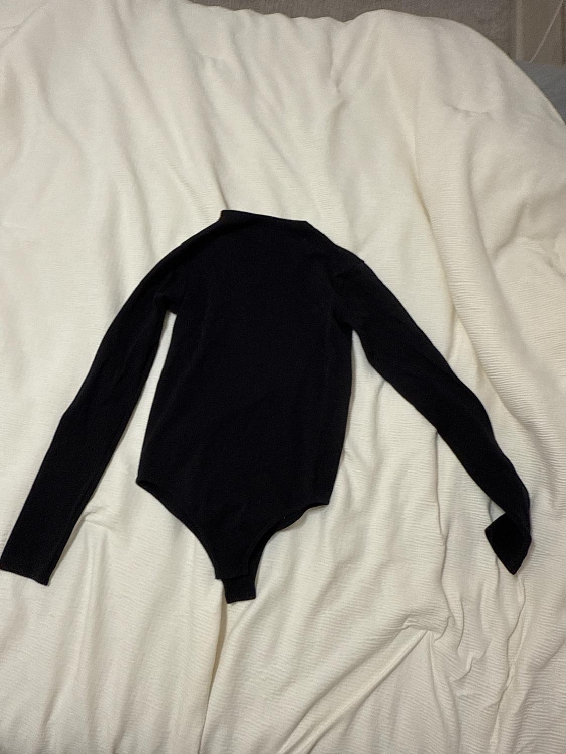 Long-sleeved black bodysuit on a bed with a white bedspread.