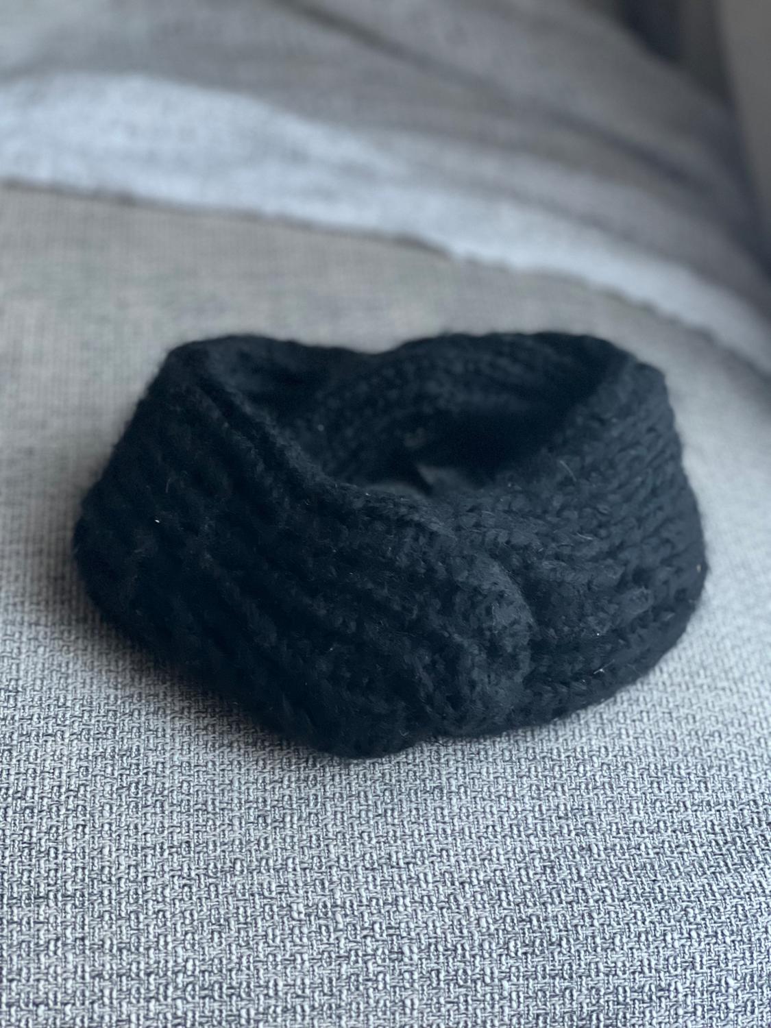 Black chunky knit scarf on a light grey sofa, with soft light coming through a nearby window.