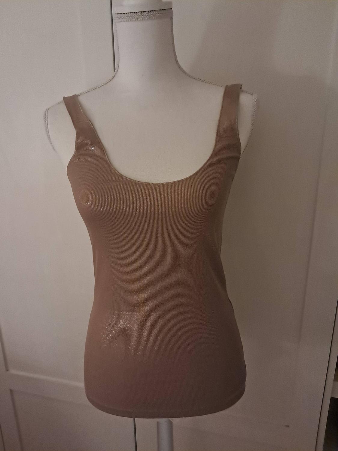 White mannequin wearing a beige ribbed vest top with a shiny finish, in front of a white door background.