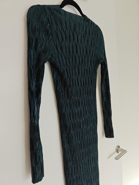 Long-sleeved dark green pleated texture maxi dress, hanging on a black hanger over a white door.