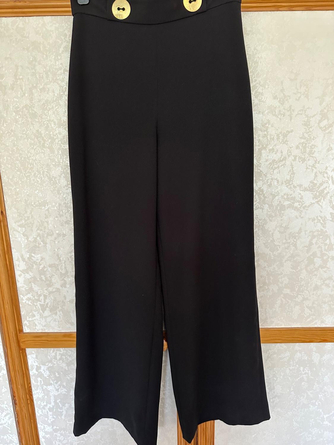 Front view of black trousers with large buttons at the waist.