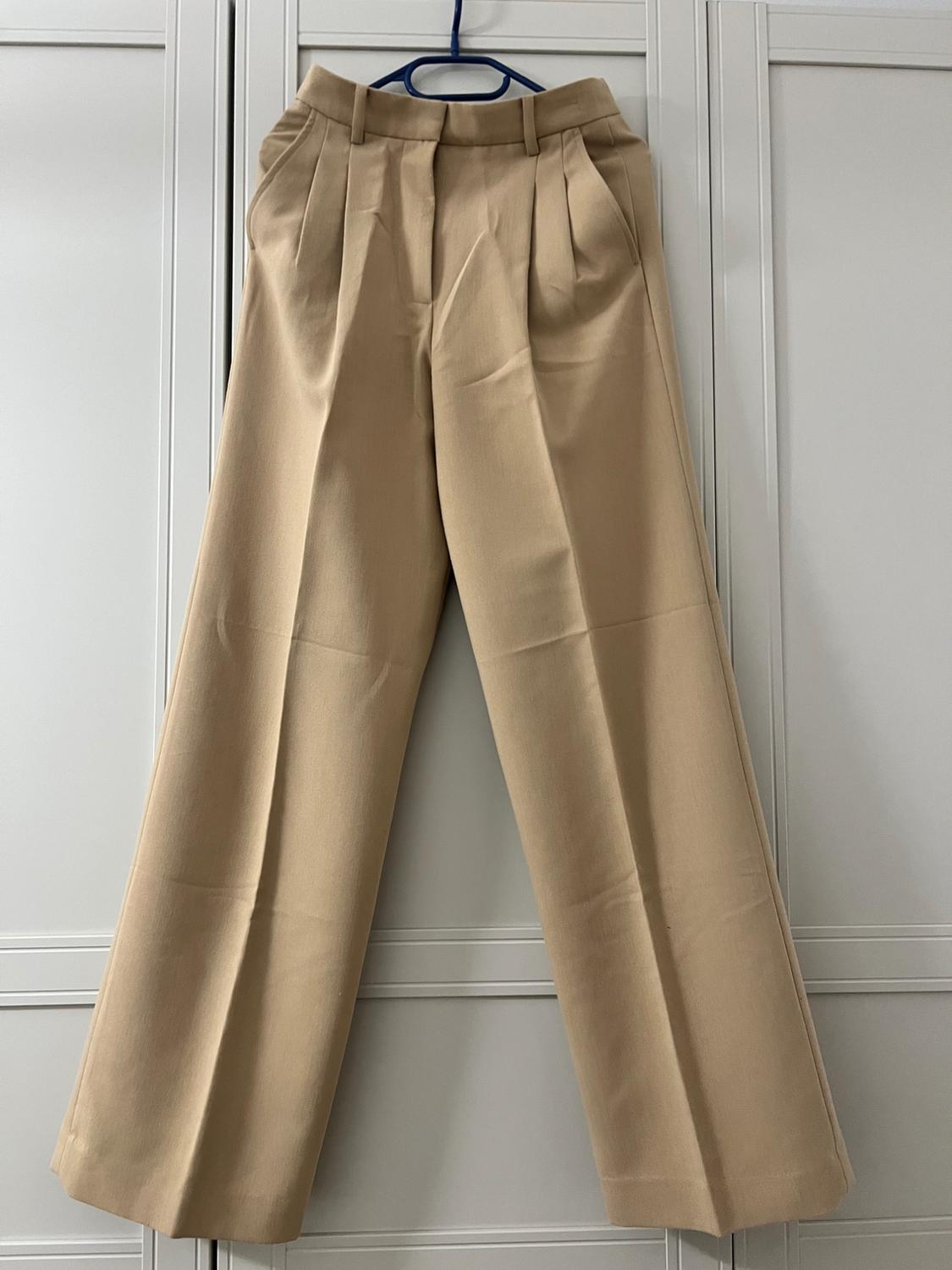 Beige wide-leg trousers hanging on a blue hanger in front of a white wardrobe.