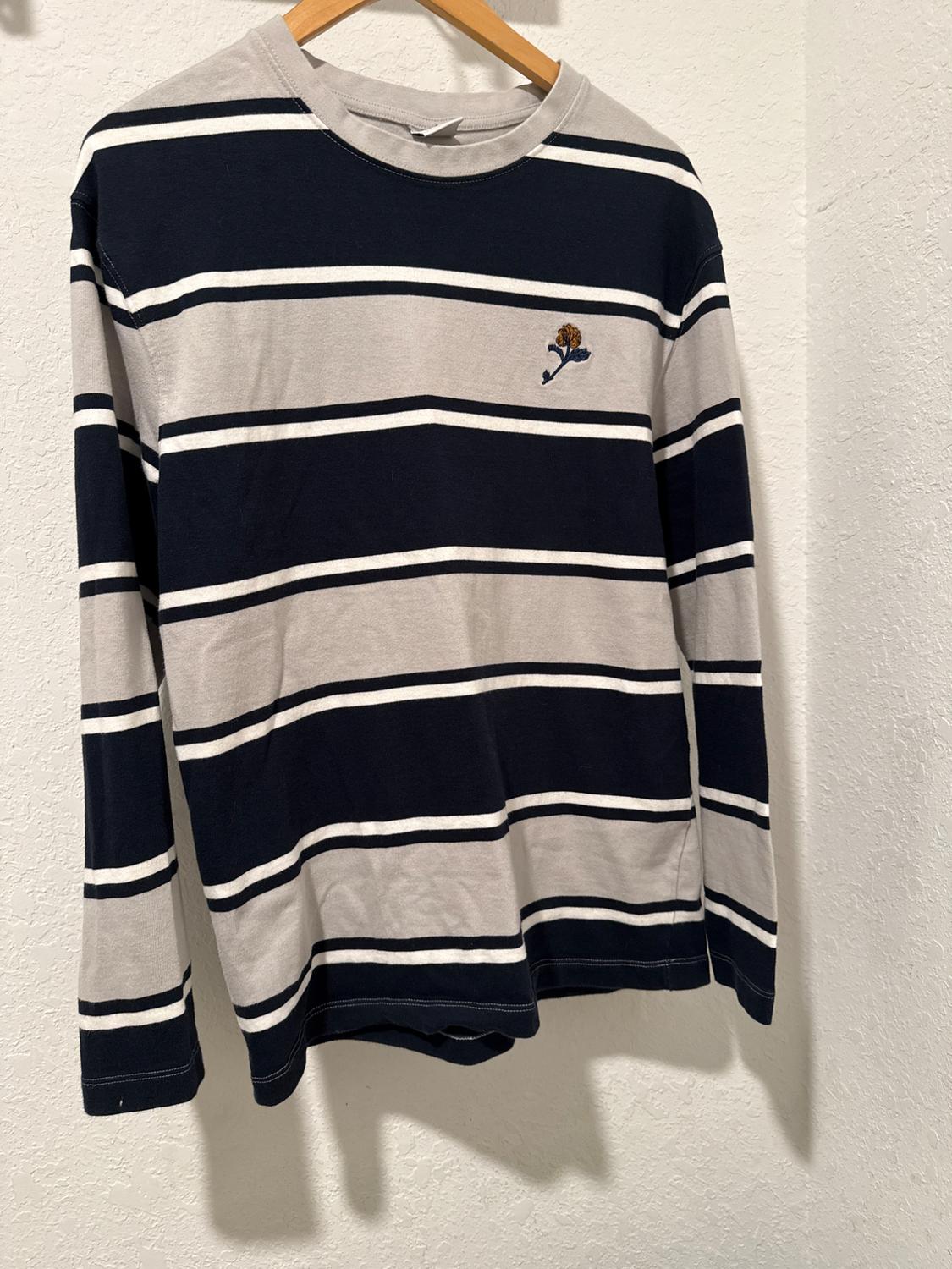 Black and grey horizontal striped T-shirt with a small flower embroidery on the chest, hanging on a wooden hanger.
