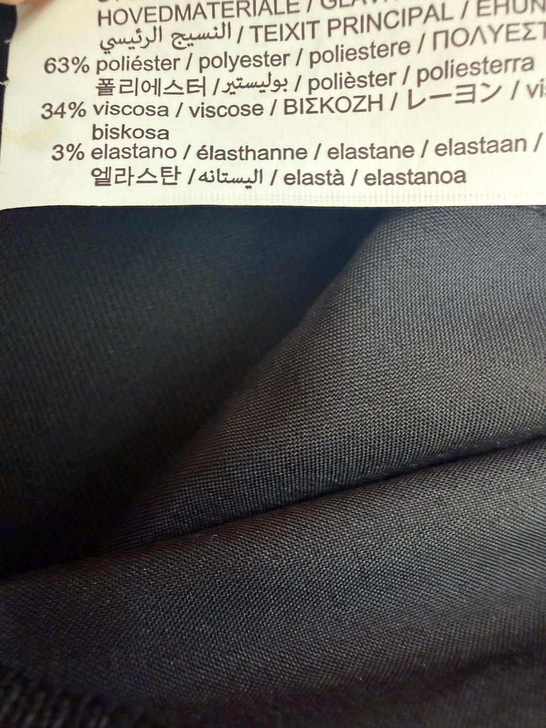 Close-up of a clothing label on dark fabric with the text: 63% polyester, 34% viscose, 3% elastane.