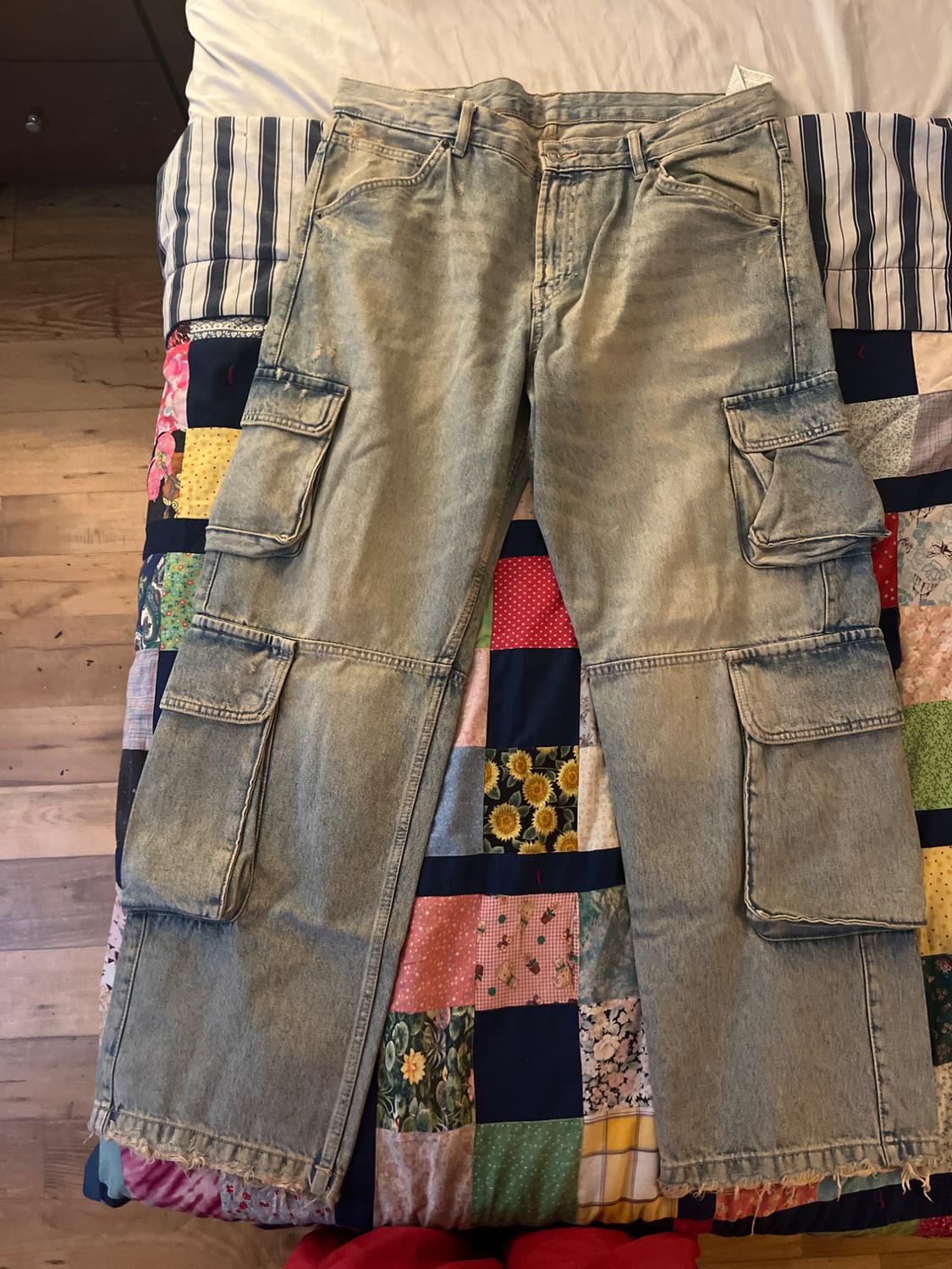 Light blue denim cargo trousers with large pockets, placed on a colourful patchwork quilt on a bed.