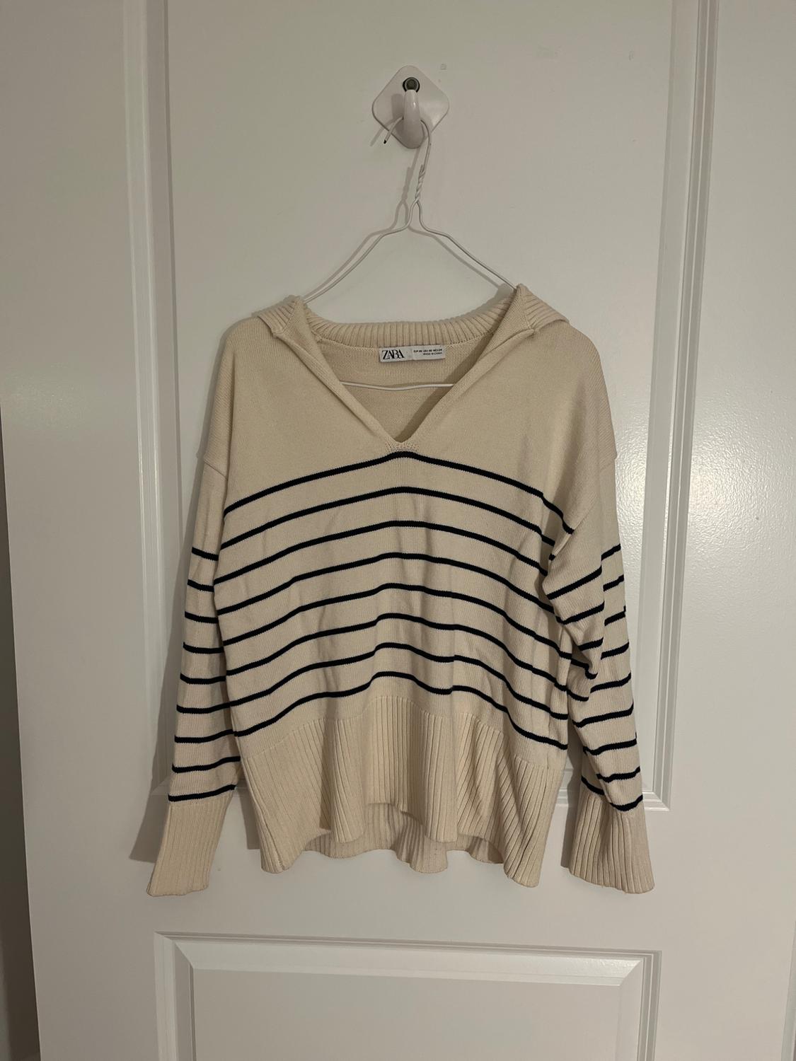 Front view of a beige jumper with black horizontal stripes and a V-neck.