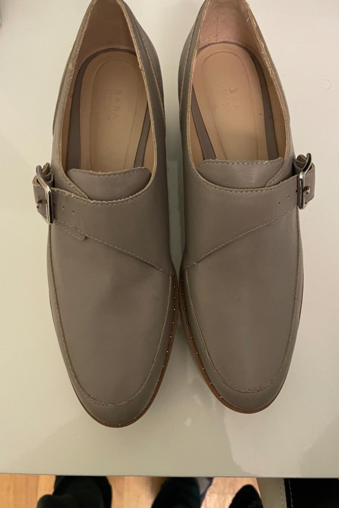 Front view of grey shoes with a metallic buckle and visible stitching.