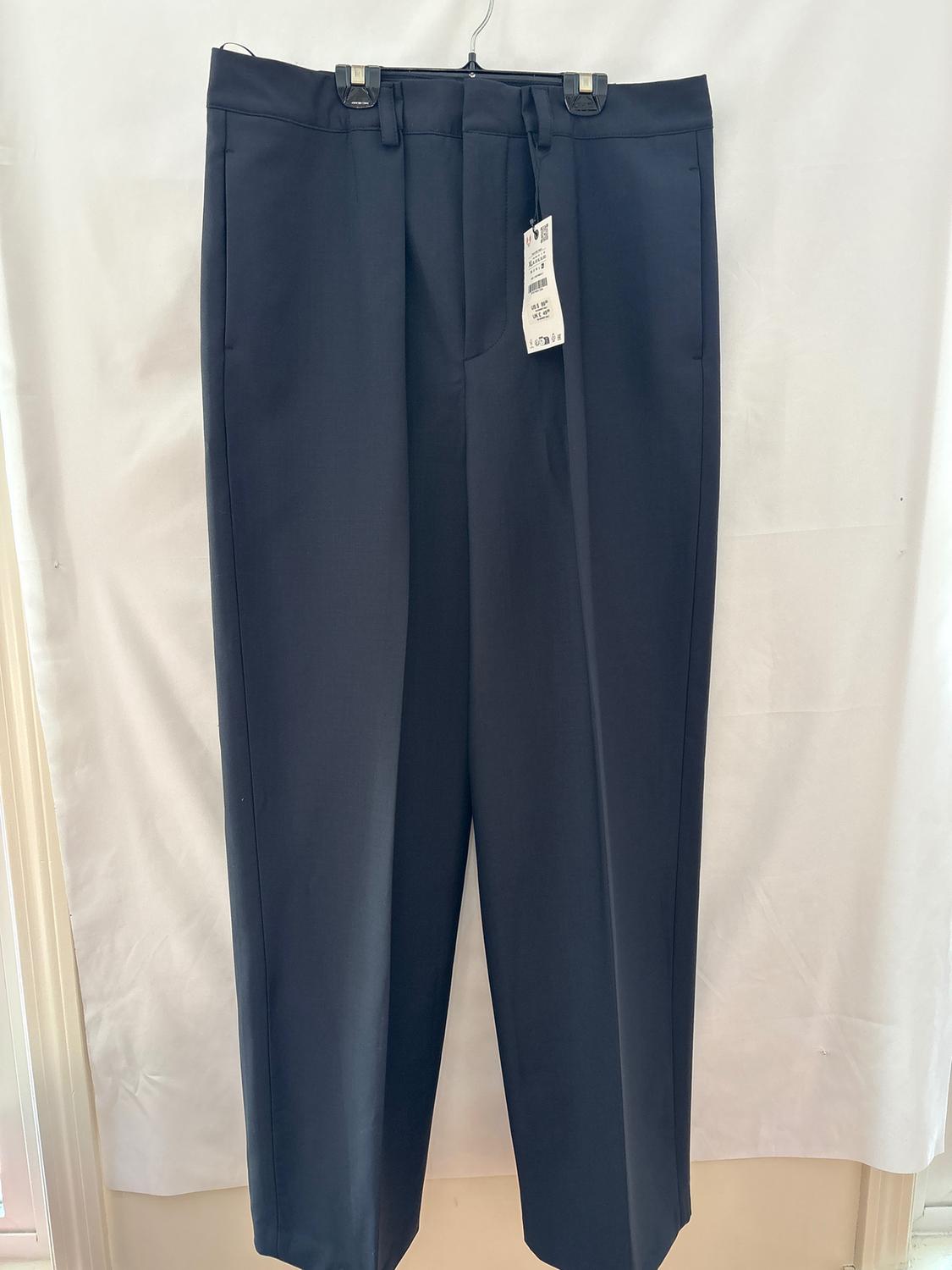 Black dress pants hanging on a hanger with visible tag, white background.