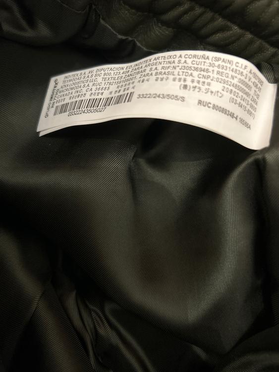 Clothing label with multi-language text on dark fabric. It reads: "INDITEX S.A. AV. DIPUTACION ED. INDITEX ARTEIXO A CORUÑA (SPAIN) C.I.F. A-15075062".