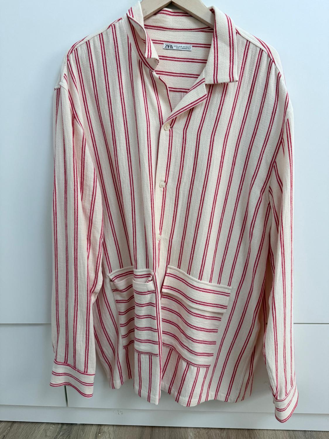 Red-and-white striped shirt hanging on a wooden hanger. Visible label: "Zara". White background and wooden floor.