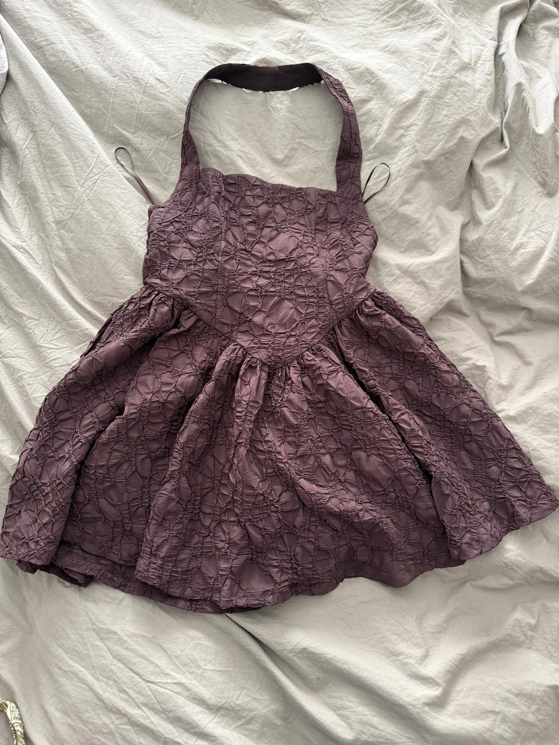 Dark purple crinkled sleeveless dress, on a wrinkled beige fabric surface.