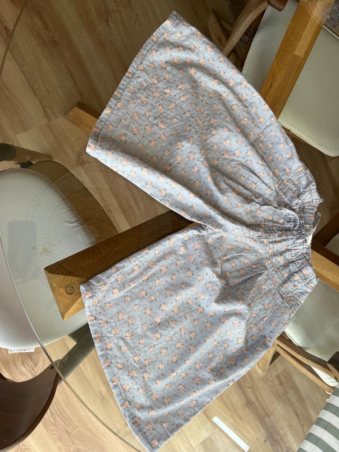 Lightweight fabric skirt with a floral pattern in pastel shades, placed on a glass table with wooden legs.