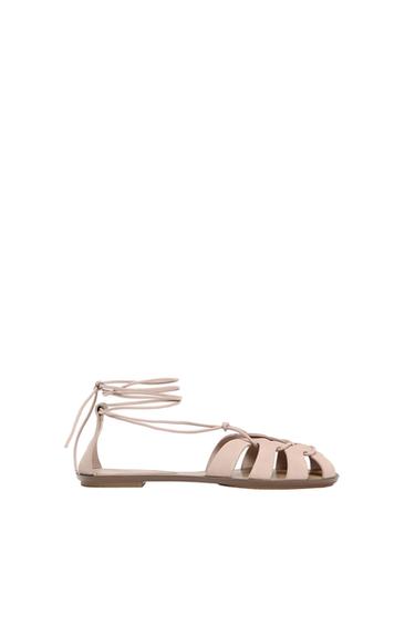 Beige flat sandals with thin ankle straps, on a white background. Minimalist and elegant design.