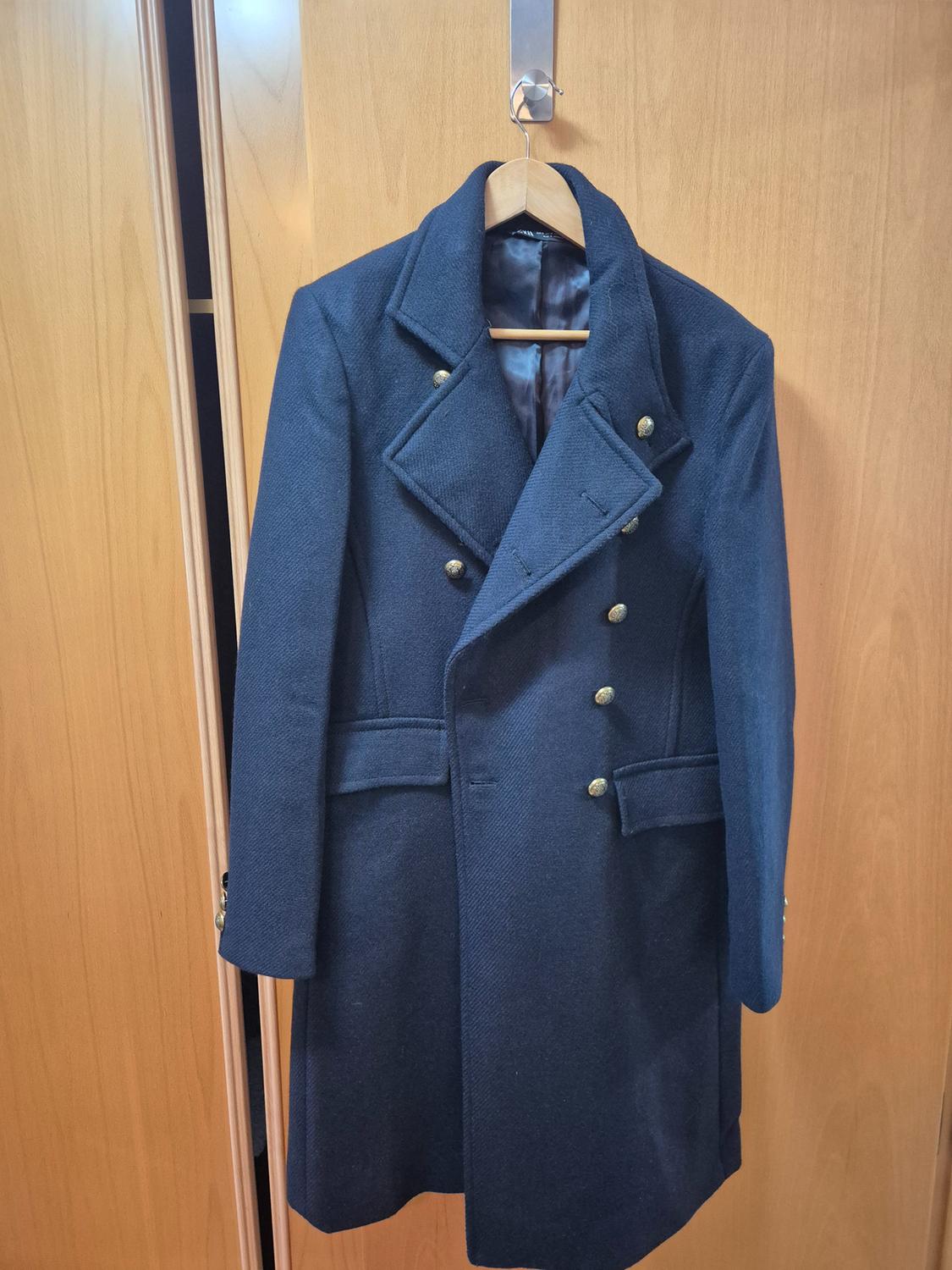 Navy blue coat with gold buttons hanging on a wooden hanger over a light wooden door.