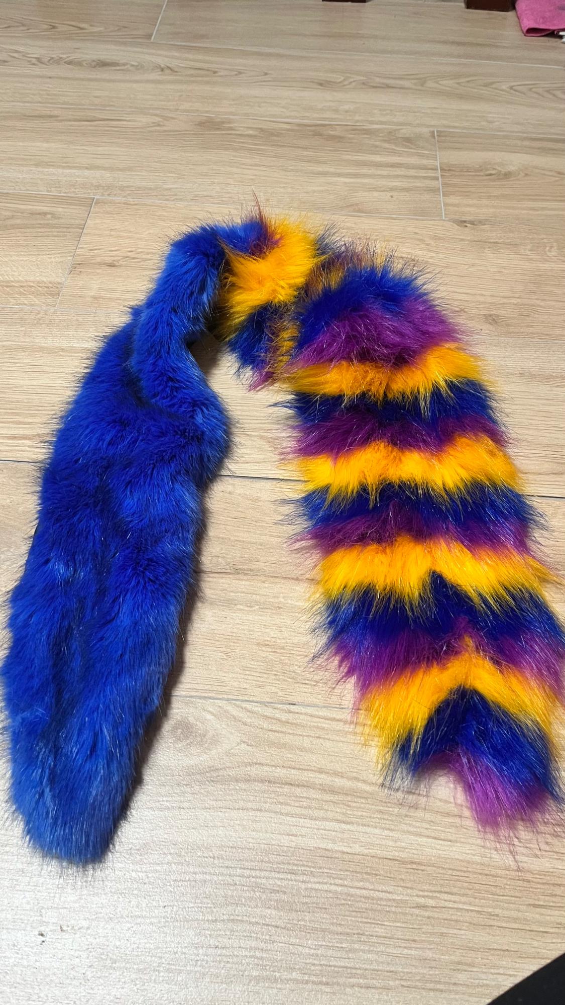 Faux fur scarf on the floor, with one blue side and the other with blue, yellow, and purple stripes.
