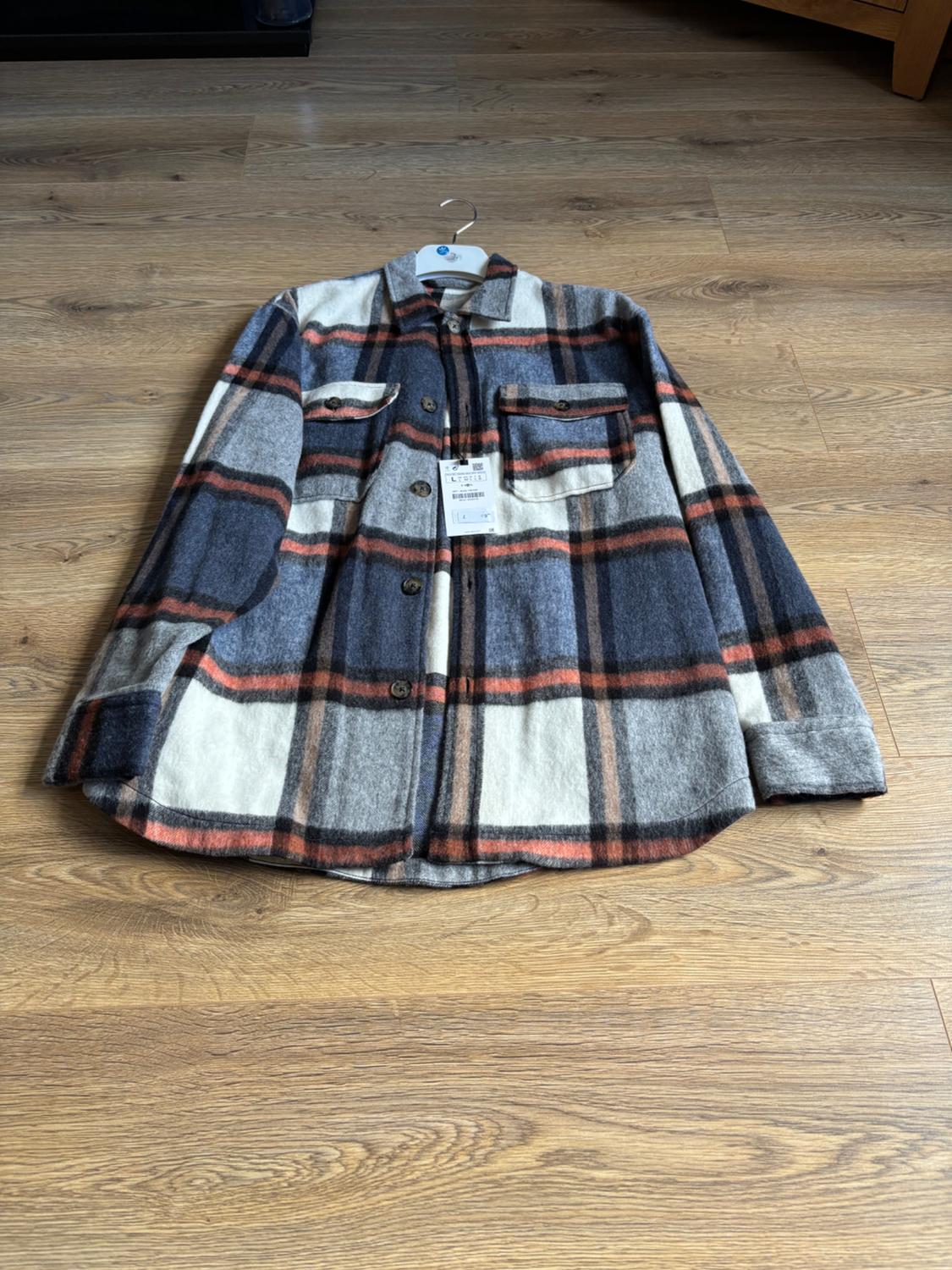 Checked shirt in shades of blue, grey, white and orange with chest pockets, hung on a clothes rail on a wooden floor.