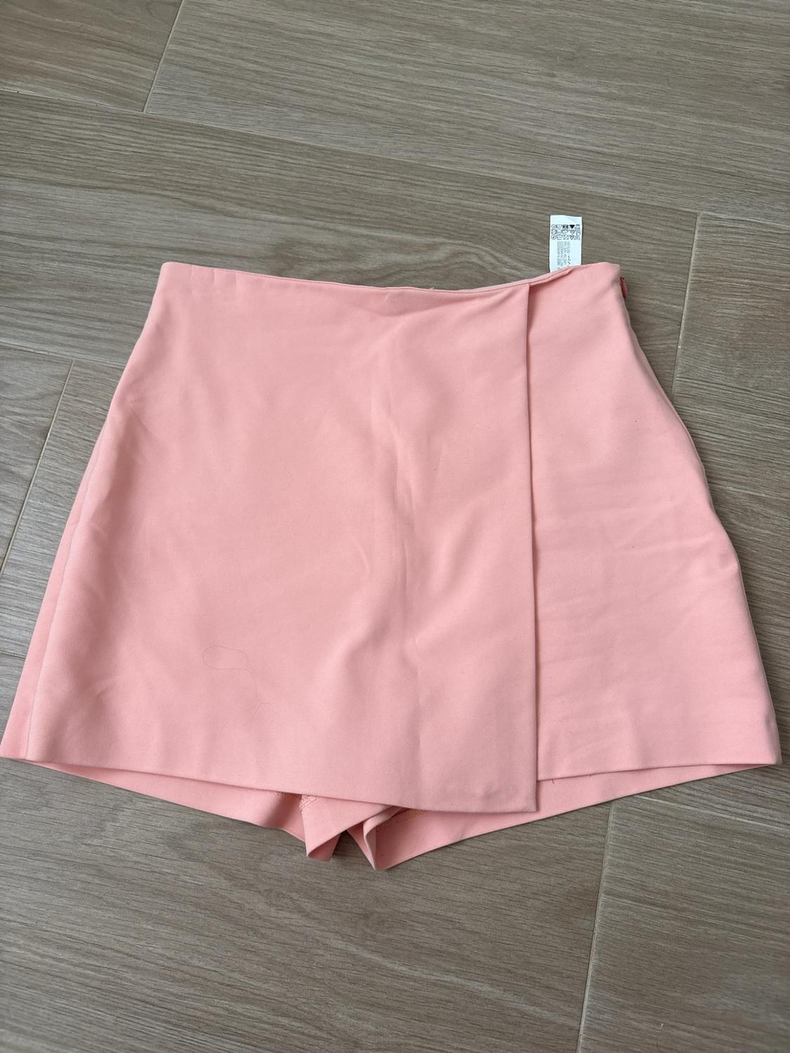 Light pink skort with overlapping front panel, laid out on a light wood floor. White label on the waistband.