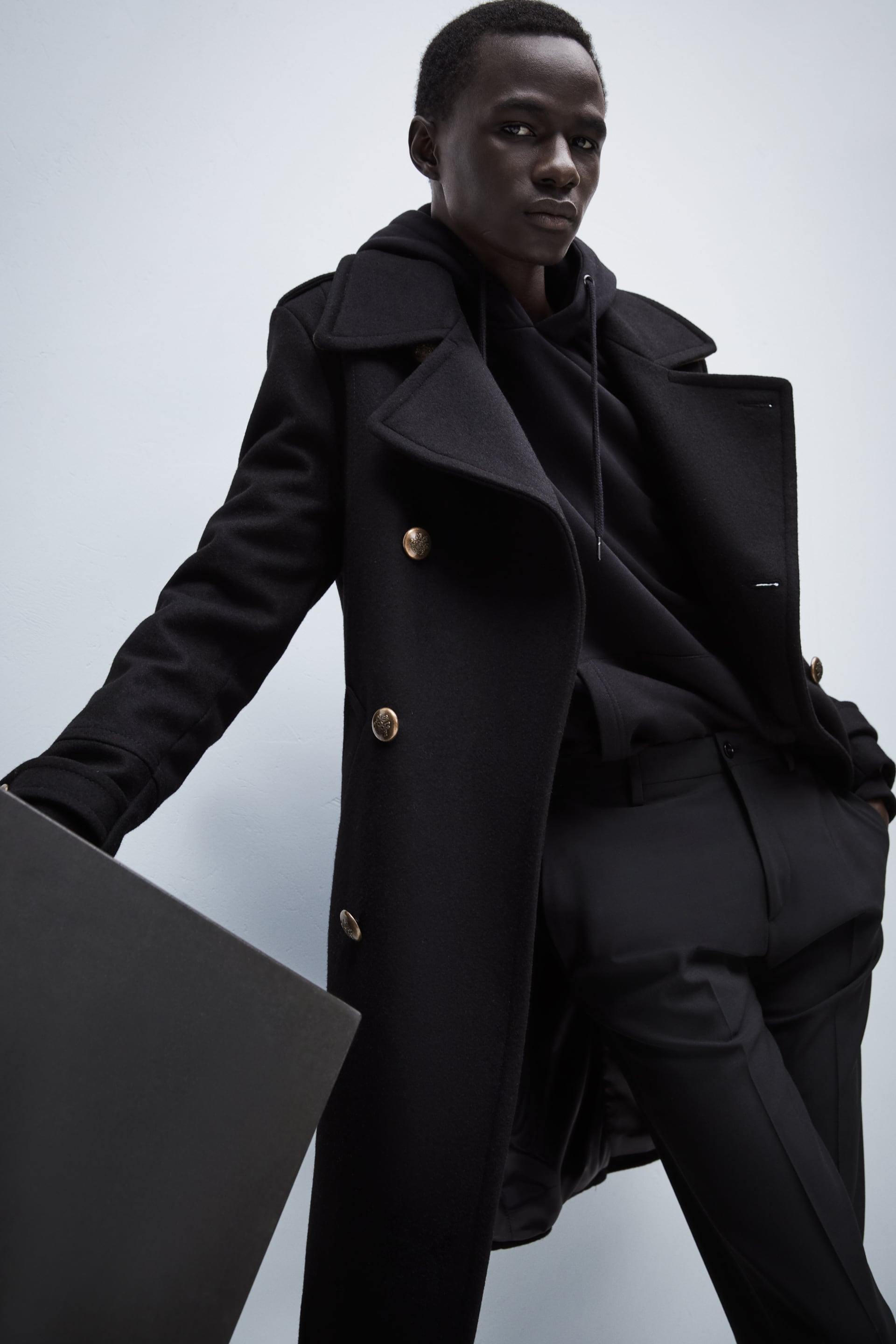 Black overcoat worn with a Black hoodie and tailored trousers.