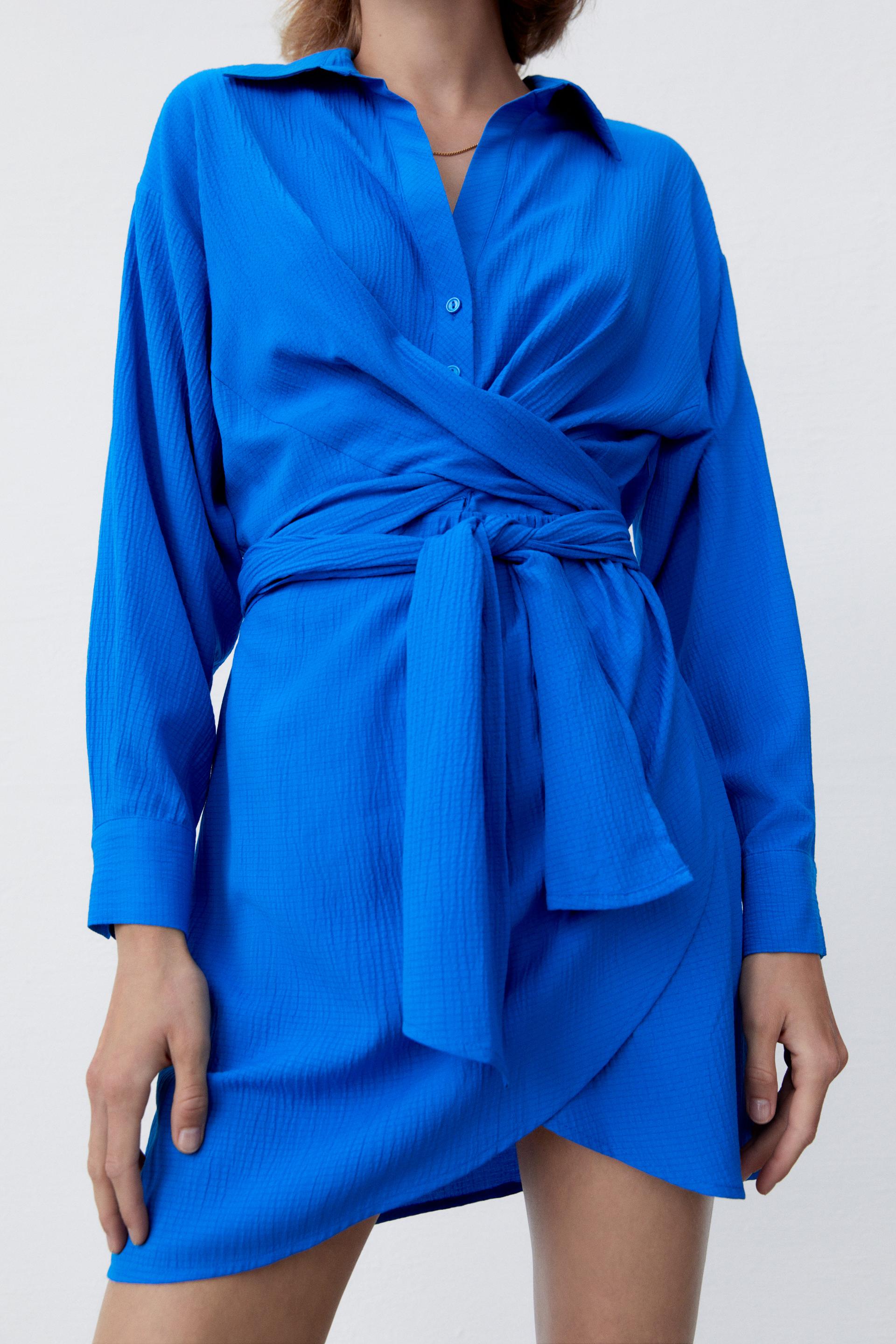 This cerulean blue Zara mini dress is a modern twist on the classic shirt dress. It has long sleeves with buttoned cuffs and a v neck and shirt collar. IT buttons up the top half, whilst the bottom is a wrap skirt with wrap around twisted tie belt offering a draped effect at the front. 