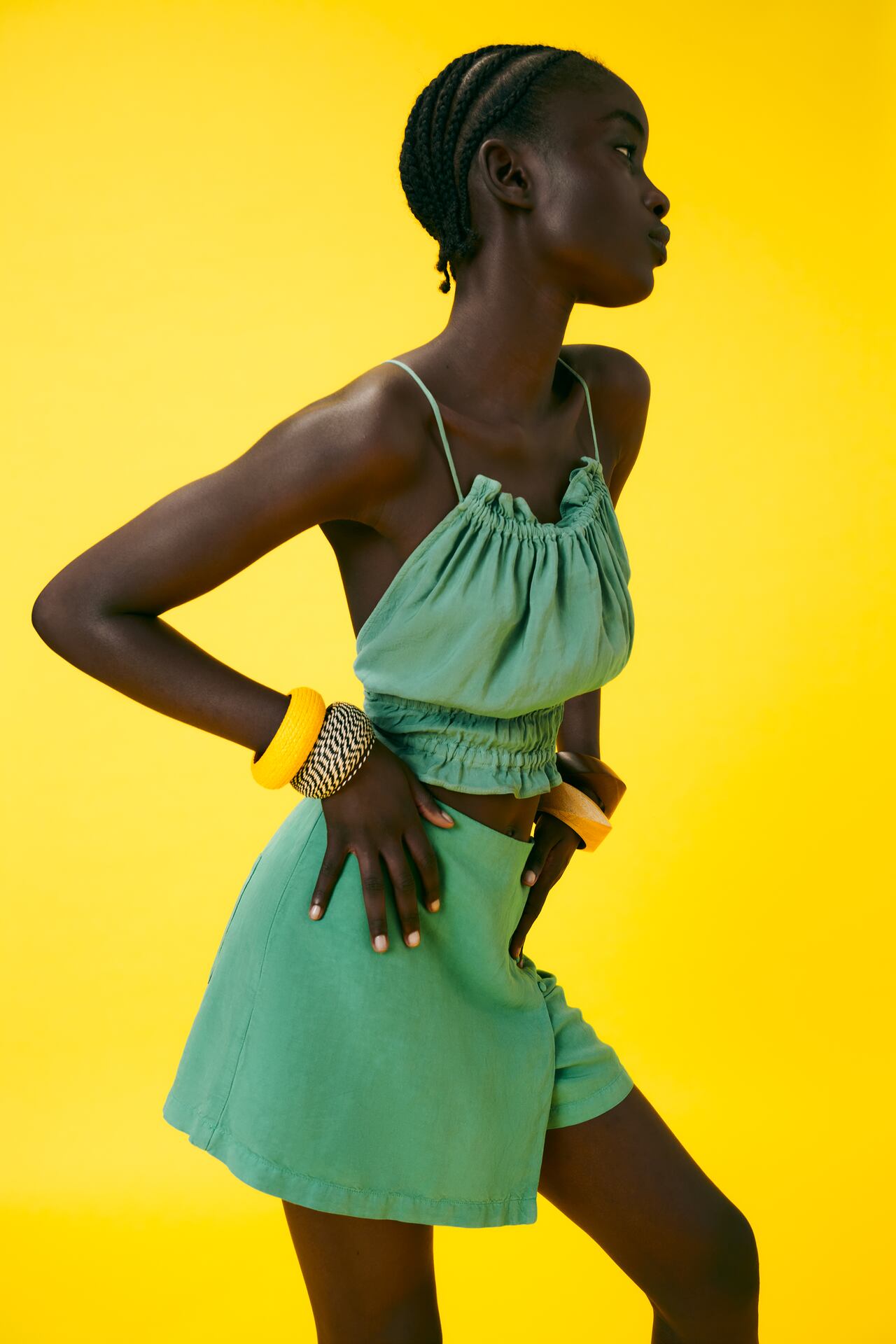Black woman wearing green strappy top and skirt against yellow background