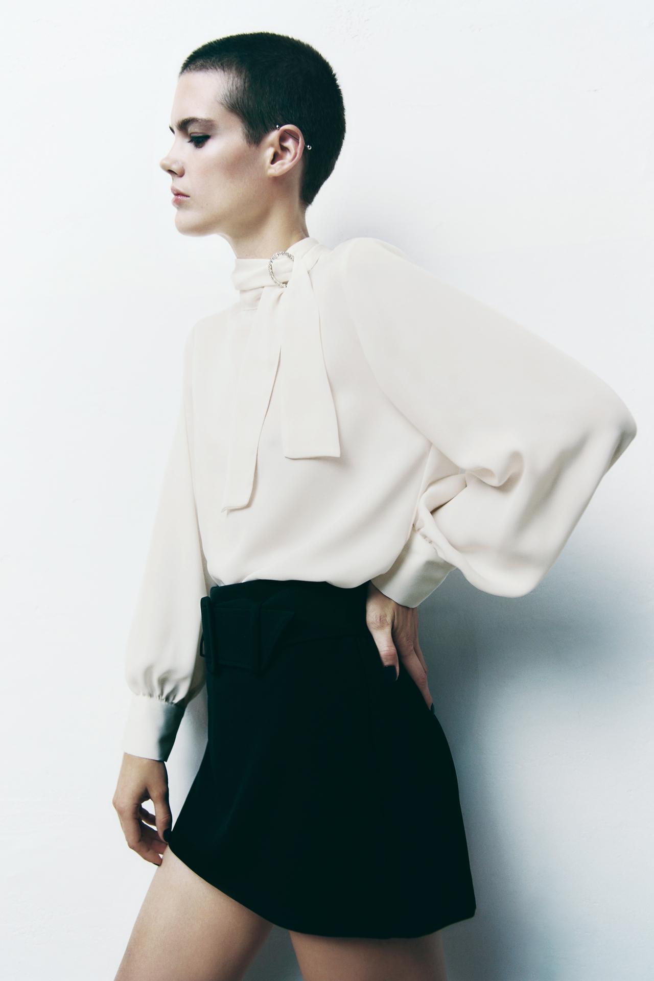 Zara oyster white coloured blouse featuring a high neck with a rhinestone buckle and long sleeves. Featuring side vents at the hem and a buttoned opening at the back.