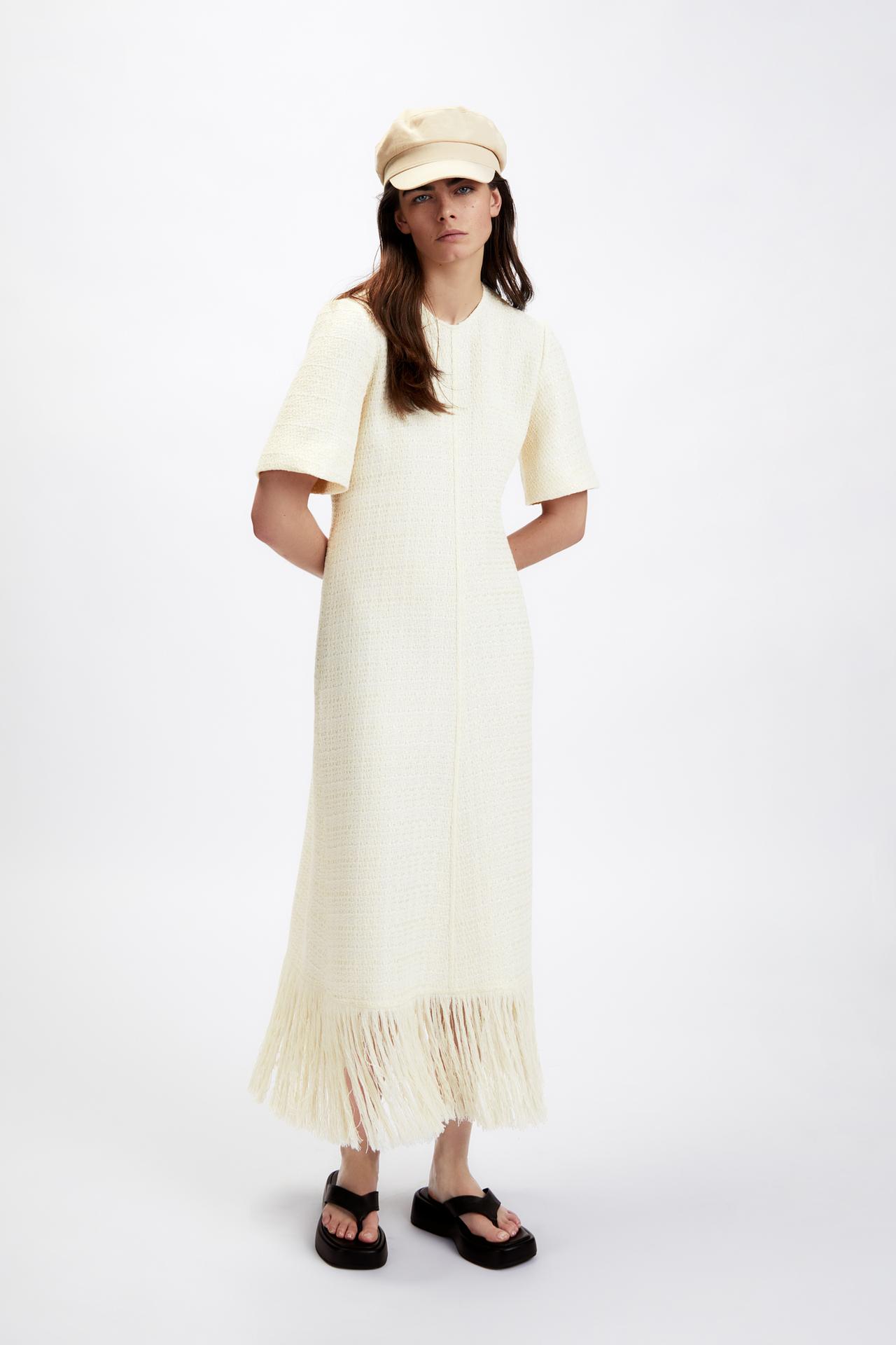 Long cream dress with a round neckline and short sleeves. Matching fringing at the hem. Invisible zip fastening at the back.