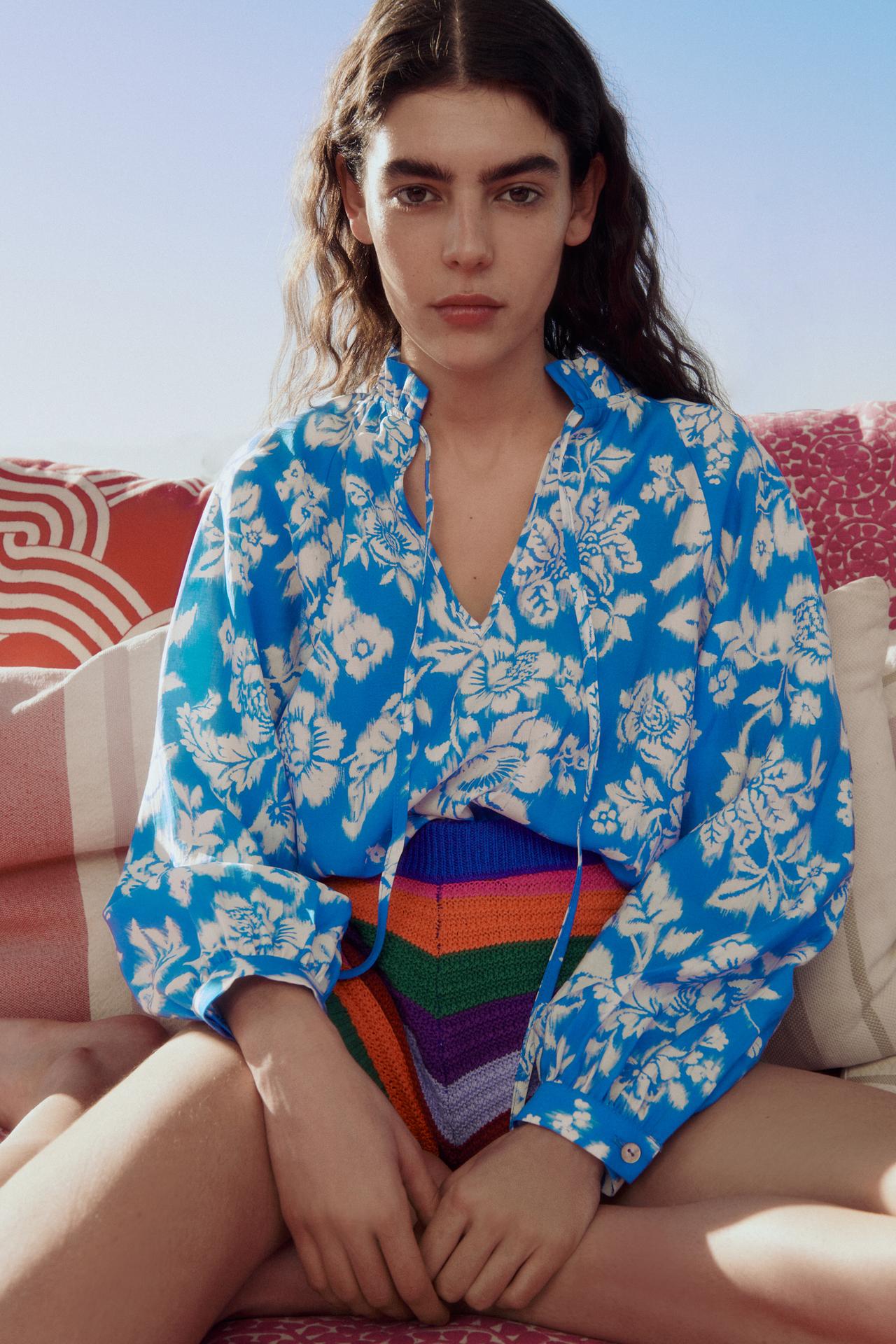 Blue and white floral print Blouse featuring a high collar with ruffles and tie. V-neckline and long sleeves.