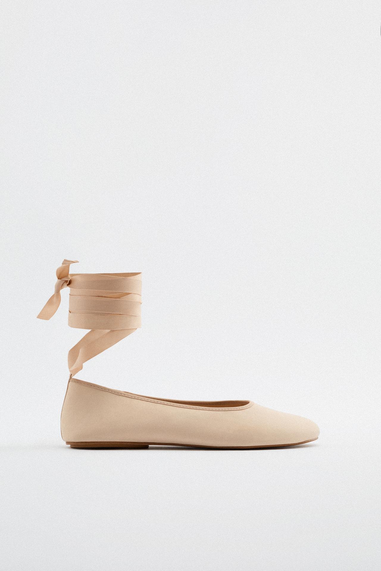 Beige fabric ballet flats. Round toe. Fastens with straps tied around the ankle.