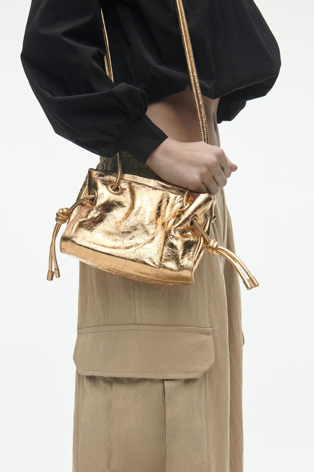 Zara gold Mini leather crossbody bag with a crackled effect. This metallic bag has tubular straps long straps that can be used as a crossbody. It has Knot details at the ends of the straps and a Zip closure.